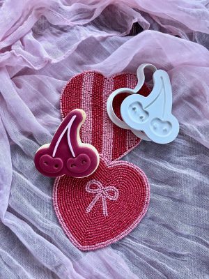 Red heart-shaped cookie with double cherry cookie cutter and fondant embosser on a pink cloth, Valentine design