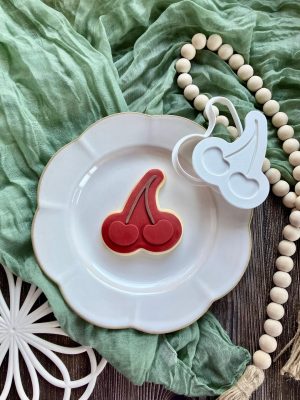 Red cherry cookie cutter and fondant embosser on white plate with green cloth