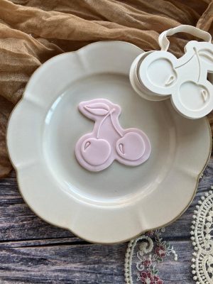 Pink double-cherry cookie cutter and fondant embosser on plate